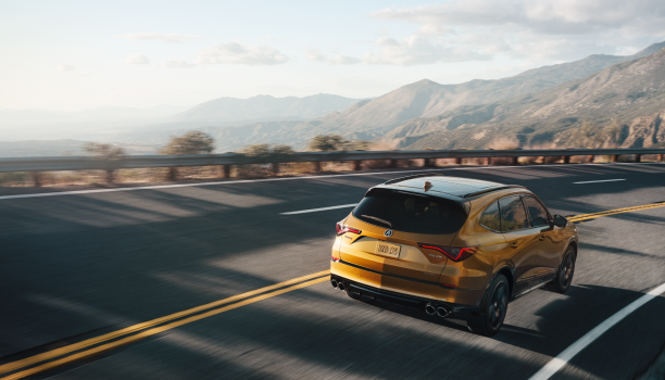 Plan étendu de trois quarts arrière d’un MDX Type S effectuant un virage sur une autoroute de montagne dans la lumière de fin d’après-midi.
